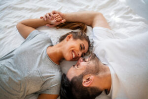 Pretty female looking at her boyfriend in bed stock photo Overhead close up of young couple lying in bed together Romantic couple in love looking at each other Smiling young couple cuddling in bed